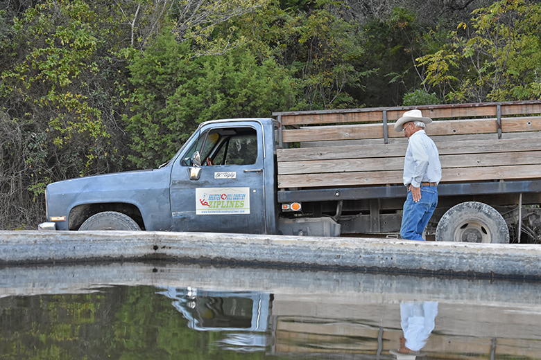 Ralph Madla and Ol’ Ugly, his truck’s nickname, reflect off the ranch’s pila. Pilas are are concrete tanks used by ranchers to hold water for their livestock. Photo by Aaron Perez