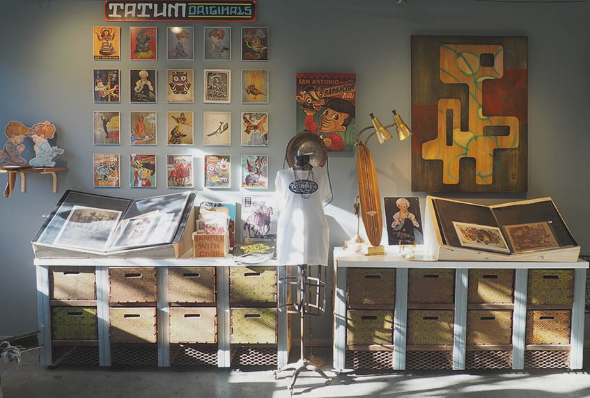 Gallery wall inside of Choice Goods, displaying prints of orginal works by Robert Tatum. Tatum's work is described as "low brow contemporary," with a tongue-in-cheek nod to pop culture. Tatum takes a break from art and reorganizing his shop/studio space to grab a cup of coffee from Halycon and enjoy a cigarette. "The art is easy, it's the business part that's hard," he said. Photo by Betty Wright Rueda
